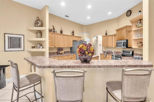 kitchen featuring kitchen peninsula, a breakfast bar, stainless steel appliances, light brown cabinets, and light tile patterned floors