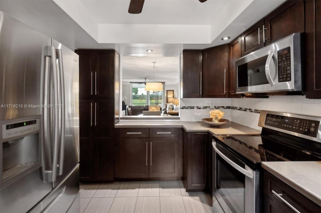 kitchen featuring light tile patterned flooring, a raised ceiling, decorative backsplash, pendant lighting, and appliances with stainless steel finishes