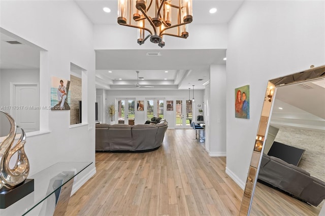 entryway with a high ceiling, ceiling fan with notable chandelier, a tray ceiling, and light hardwood / wood-style floors