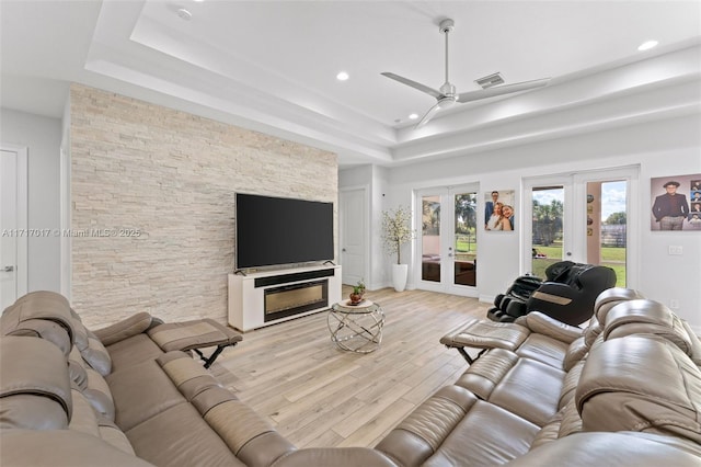 living room with ceiling fan, a fireplace, a tray ceiling, and french doors