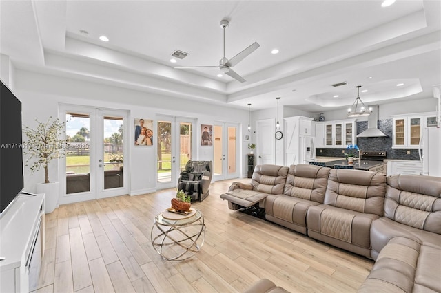 living room with french doors, a tray ceiling, ceiling fan, and light hardwood / wood-style floors