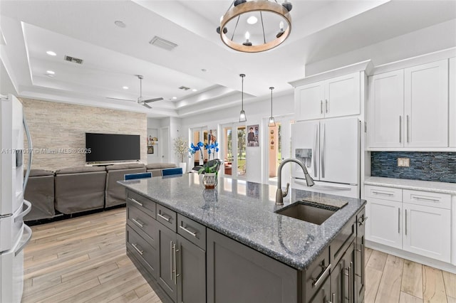 kitchen with white refrigerator with ice dispenser, a tray ceiling, white cabinetry, and ceiling fan