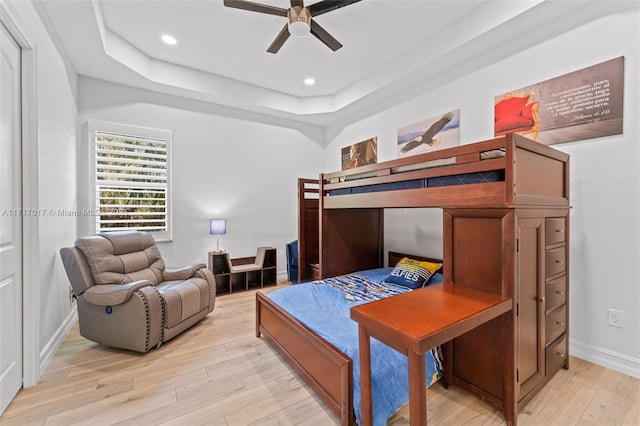 bedroom with ceiling fan, a raised ceiling, and light wood-type flooring