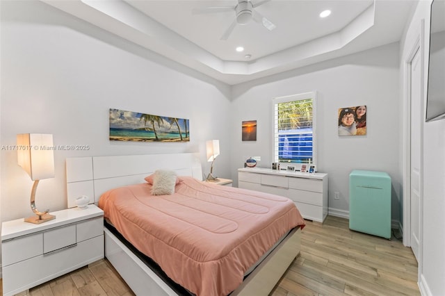 bedroom with a tray ceiling, light hardwood / wood-style flooring, and ceiling fan