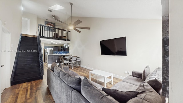 living room featuring ceiling fan, vaulted ceiling with skylight, and hardwood / wood-style floors