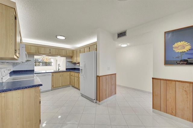 kitchen featuring sink, a textured ceiling, white appliances, wooden walls, and light brown cabinetry