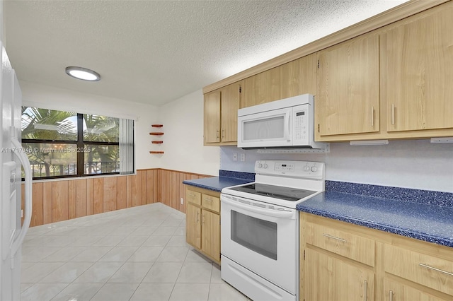 kitchen featuring light brown cabinets, wood walls, white appliances, light tile patterned floors, and a textured ceiling