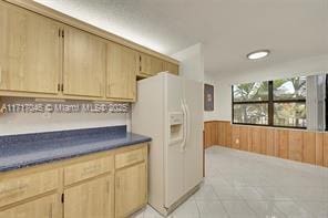 kitchen with wood walls, light brown cabinetry, and white refrigerator with ice dispenser