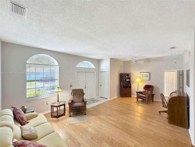 living room with ceiling fan, a textured ceiling, and light wood-type flooring