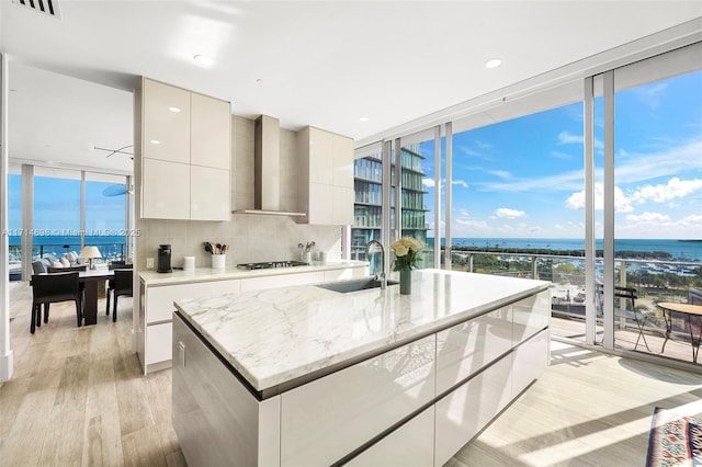 kitchen featuring sink, stainless steel gas cooktop, a water view, wall chimney range hood, and white cabinets