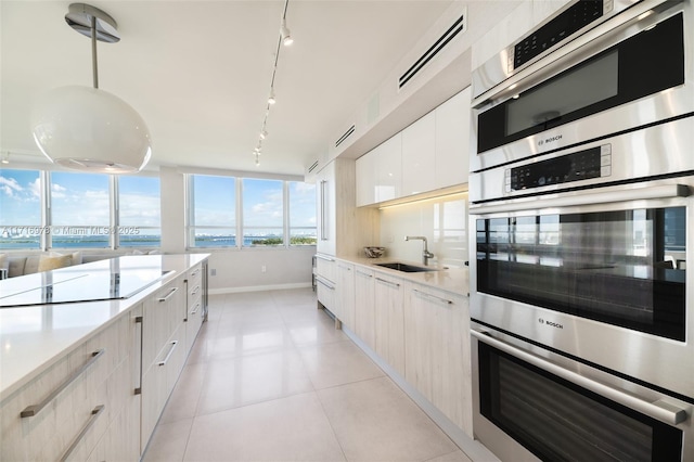 kitchen featuring black electric stovetop, double oven, sink, white cabinetry, and hanging light fixtures