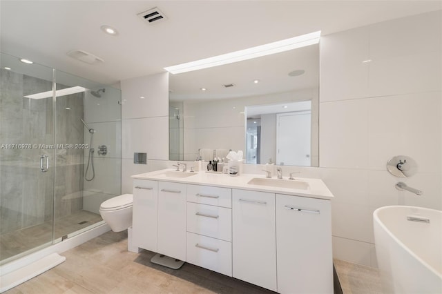 full bathroom with double vanity, a stall shower, visible vents, a freestanding bath, and a sink
