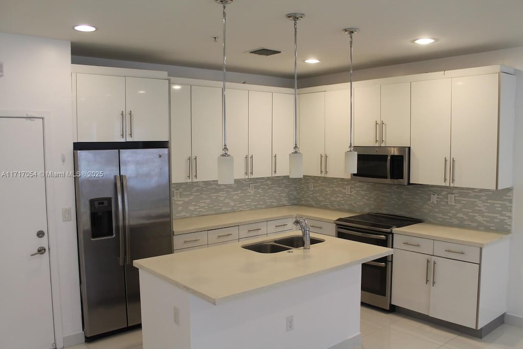 kitchen featuring white cabinetry, sink, stainless steel appliances, an island with sink, and pendant lighting