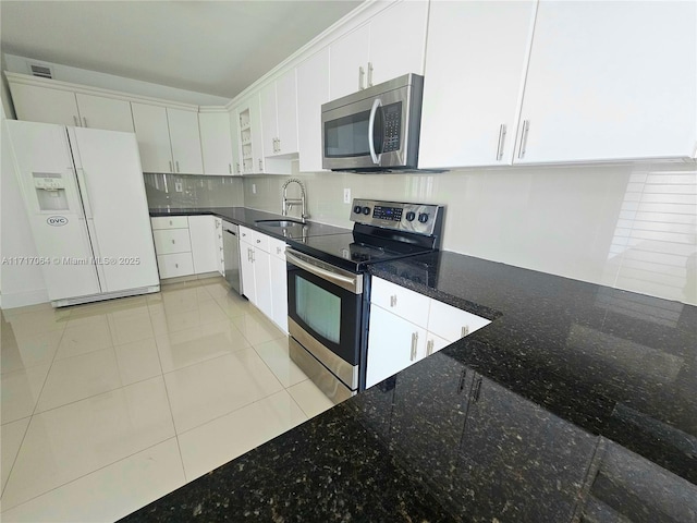 kitchen with a sink, dark stone countertops, tasteful backsplash, appliances with stainless steel finishes, and white cabinets