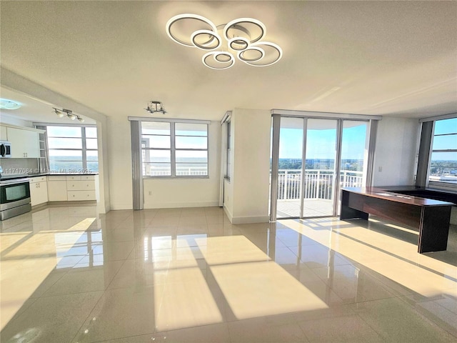 interior space with light tile patterned floors, a textured ceiling, a wall of windows, and baseboards