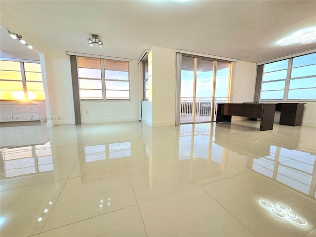 tiled empty room featuring a wall of windows, baseboards, and a healthy amount of sunlight