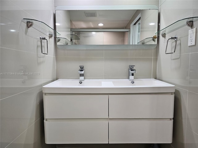 bathroom featuring tile walls, double vanity, visible vents, and a sink