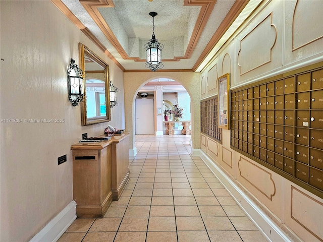 hall with crown molding, a tray ceiling, arched walkways, light tile patterned flooring, and a textured ceiling