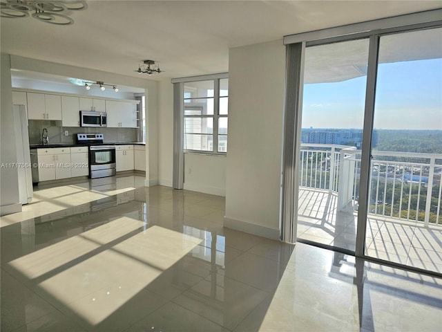 kitchen with a wall of windows, baseboards, white cabinets, appliances with stainless steel finishes, and dark countertops