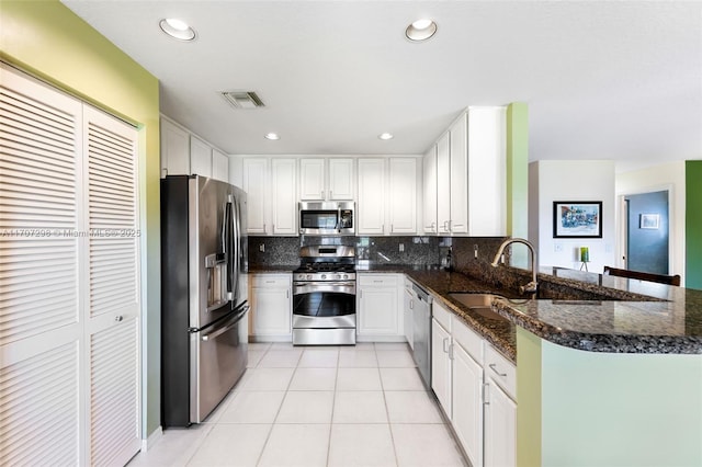 kitchen featuring kitchen peninsula, dark stone counters, stainless steel appliances, light tile patterned floors, and white cabinetry