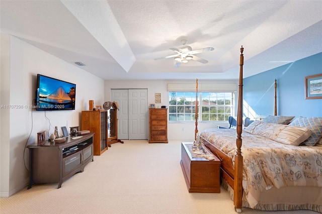 bedroom featuring ceiling fan, a raised ceiling, light colored carpet, a textured ceiling, and a closet