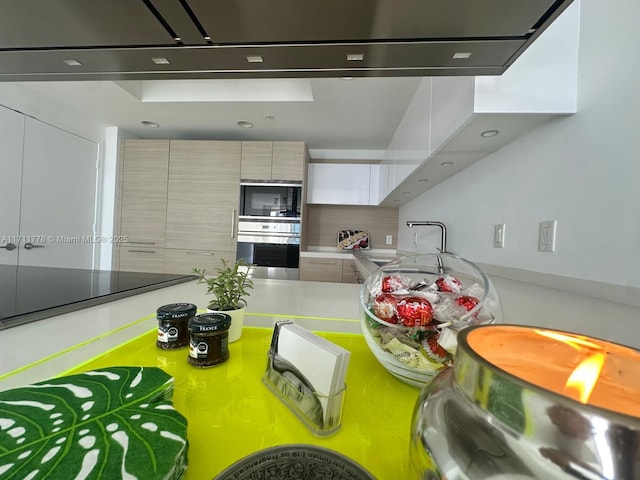 kitchen featuring black microwave, oven, a sink, light countertops, and modern cabinets