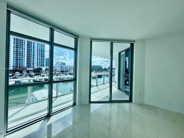 spare room featuring a wall of windows, a view of city, a water view, and baseboards