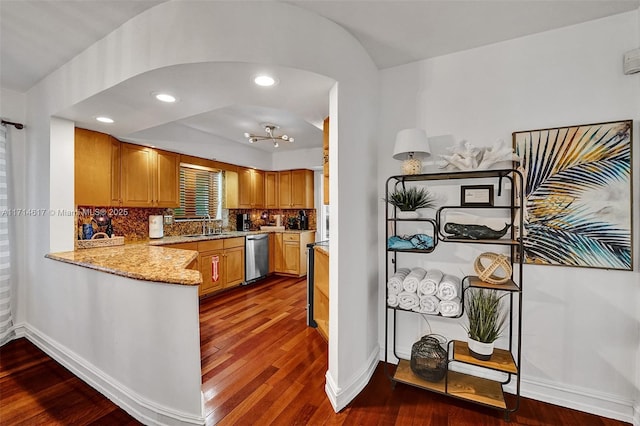 kitchen with backsplash, light stone counters, stainless steel dishwasher, dark wood-type flooring, and sink