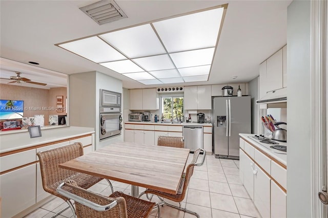 kitchen with appliances with stainless steel finishes, ceiling fan, sink, light tile patterned floors, and white cabinetry