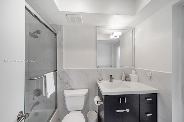 full bathroom featuring vanity, bath / shower combo with glass door, tile walls, and toilet