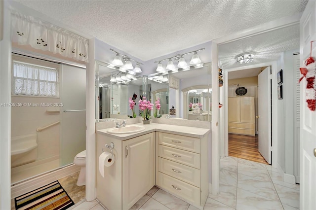 bathroom featuring a textured ceiling, toilet, walk in shower, and vanity