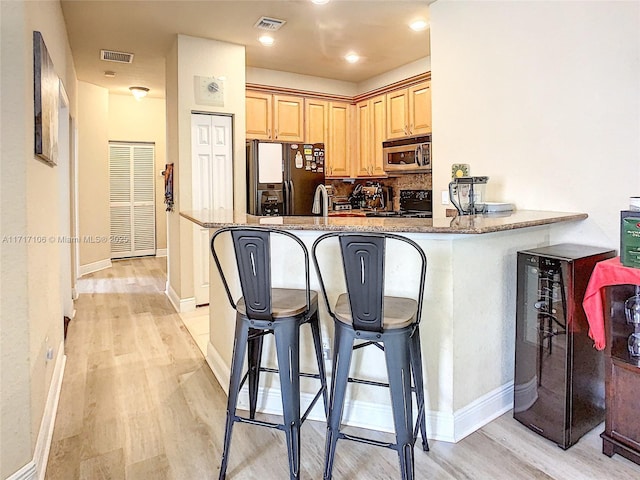 kitchen with a breakfast bar area, kitchen peninsula, light brown cabinetry, and black appliances