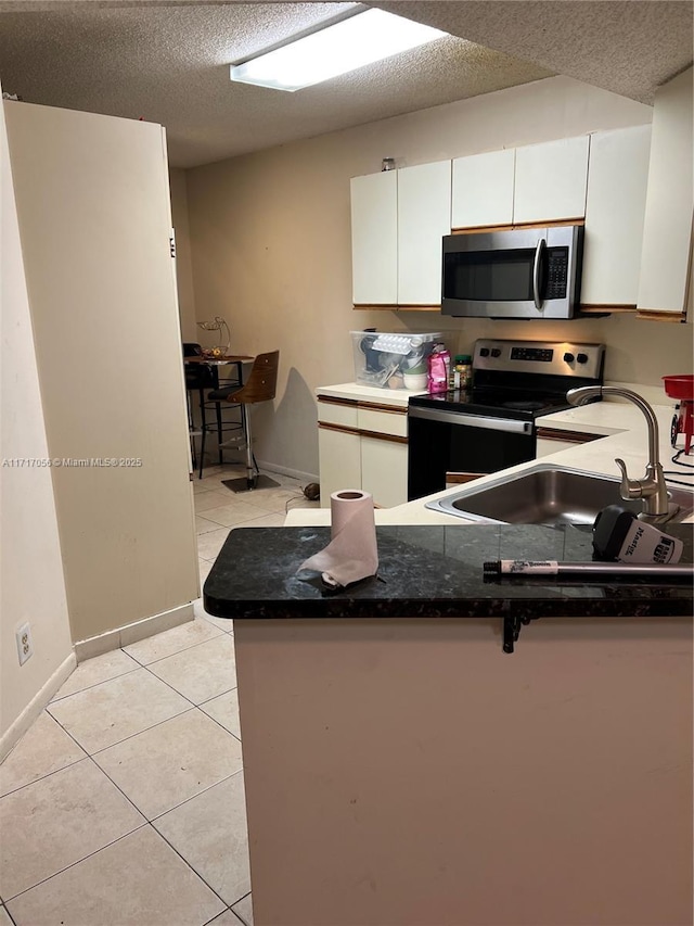 kitchen with kitchen peninsula, appliances with stainless steel finishes, light tile patterned floors, and sink