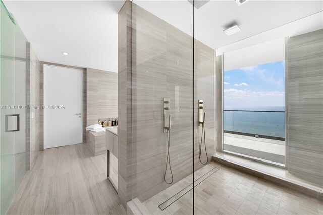 bathroom featuring shower with separate bathtub, a water view, and tile walls