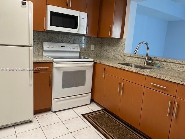 kitchen featuring backsplash, sink, light tile patterned floors, and white appliances