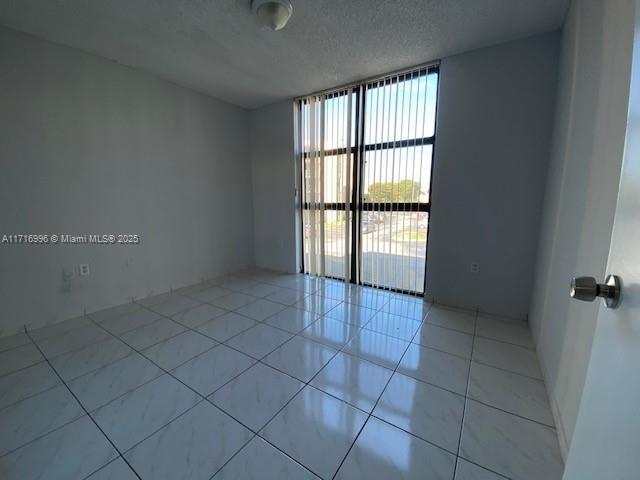 tiled empty room featuring a wall of windows