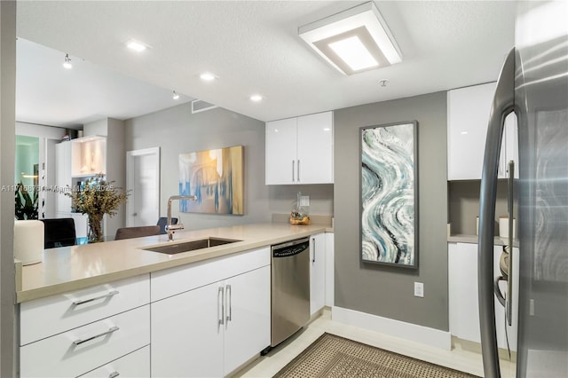 kitchen featuring refrigerator, stainless steel dishwasher, a textured ceiling, sink, and white cabinets