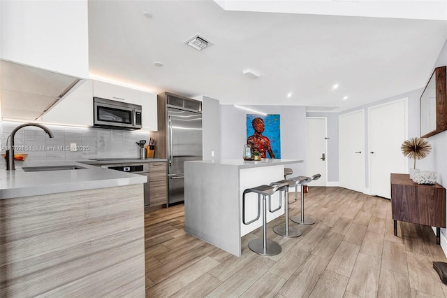 kitchen with white cabinets, sink, appliances with stainless steel finishes, tasteful backsplash, and a breakfast bar area