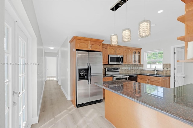 kitchen with tasteful backsplash, stainless steel appliances, sink, decorative light fixtures, and dark stone countertops