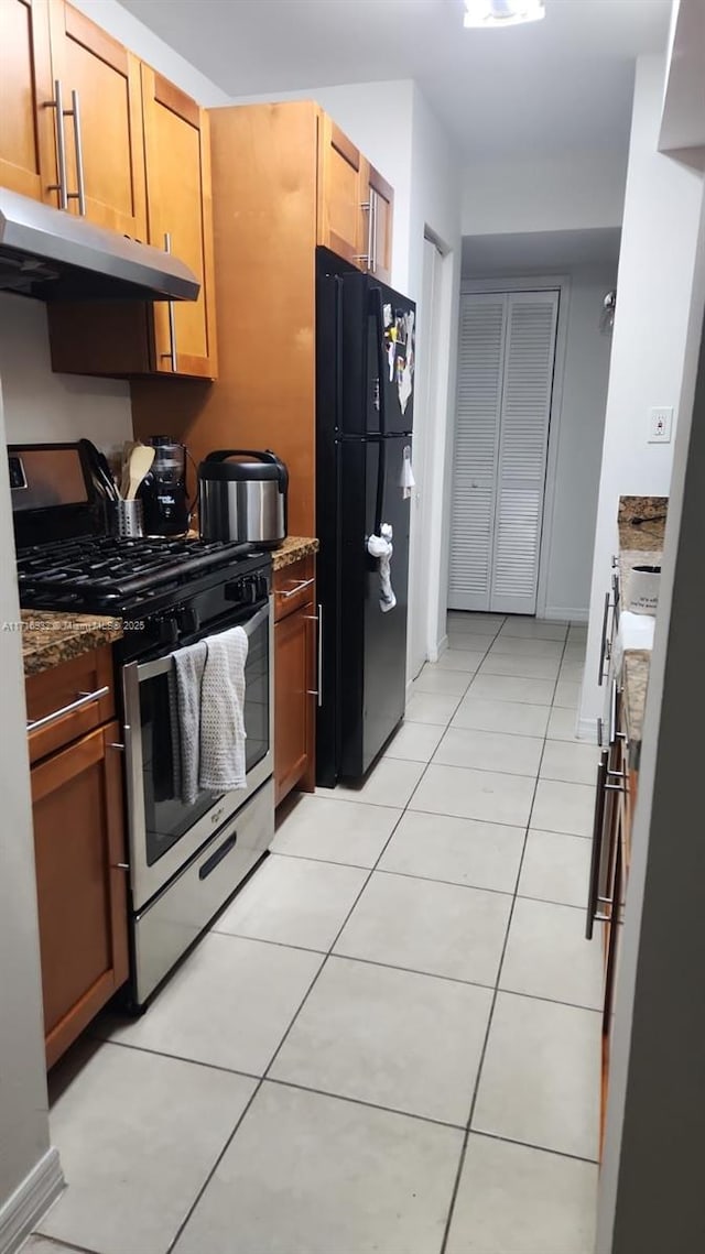 kitchen featuring black fridge, stainless steel gas stove, light tile patterned flooring, and dark stone counters