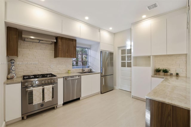 kitchen with wall chimney exhaust hood, modern cabinets, a sink, and appliances with stainless steel finishes