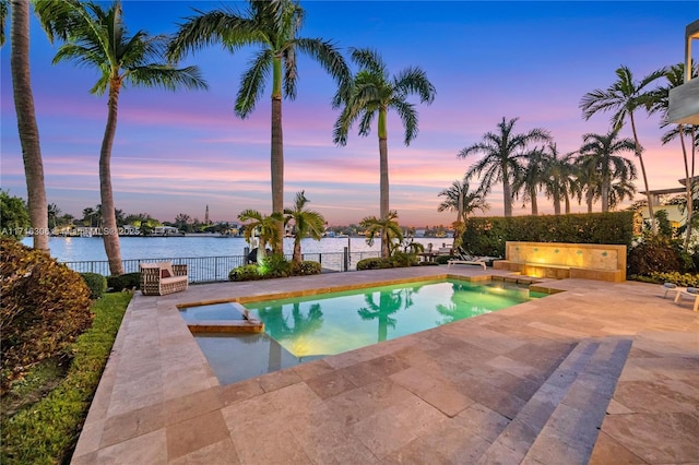 pool at dusk featuring a water view and a patio area