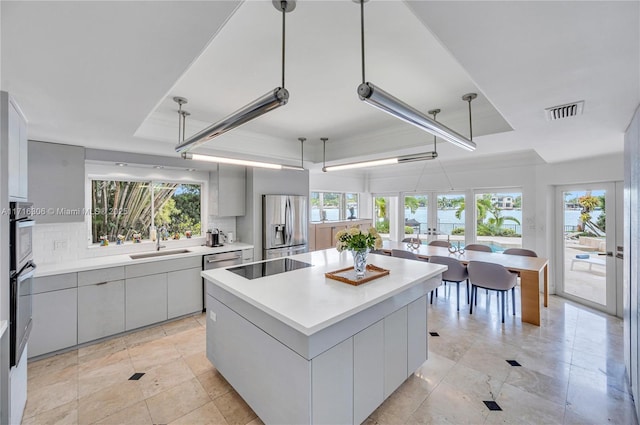 kitchen featuring a center island, sink, stainless steel appliances, pendant lighting, and a tray ceiling