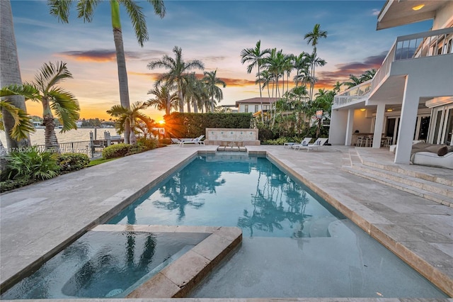 pool at dusk with a water view, a patio, and an in ground hot tub