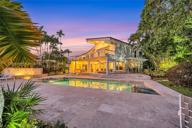 pool at dusk featuring a patio and a hot tub