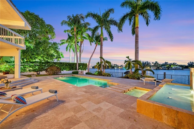 pool at dusk featuring an in ground hot tub, a water view, and a patio