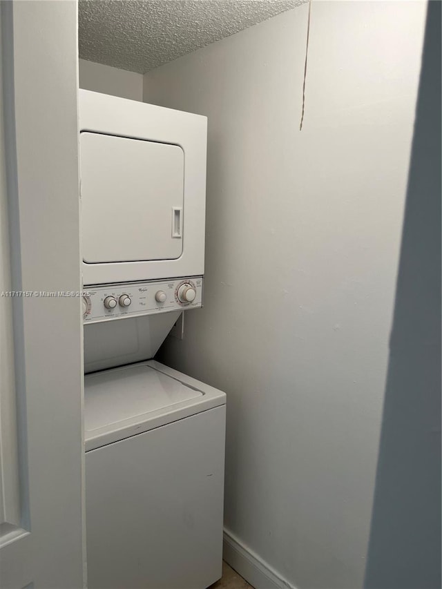 clothes washing area featuring a textured ceiling and stacked washer / dryer