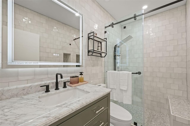 bathroom with a shower with door, tile walls, vanity, decorative backsplash, and toilet