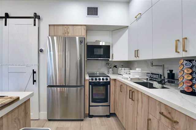 kitchen with white cabinetry, backsplash, stainless steel appliances, light stone counters, and a barn door