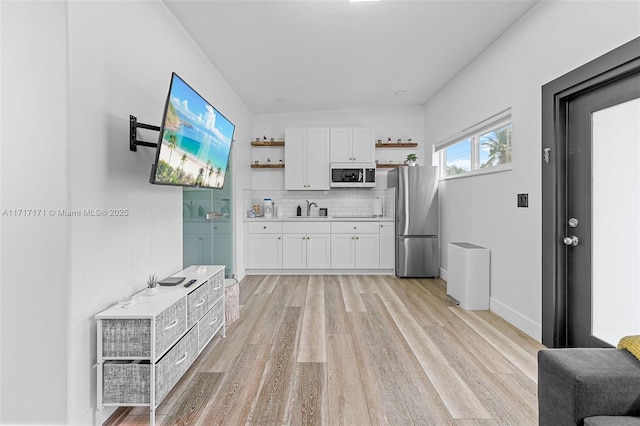 kitchen with stainless steel refrigerator, tasteful backsplash, white cabinetry, sink, and light hardwood / wood-style flooring